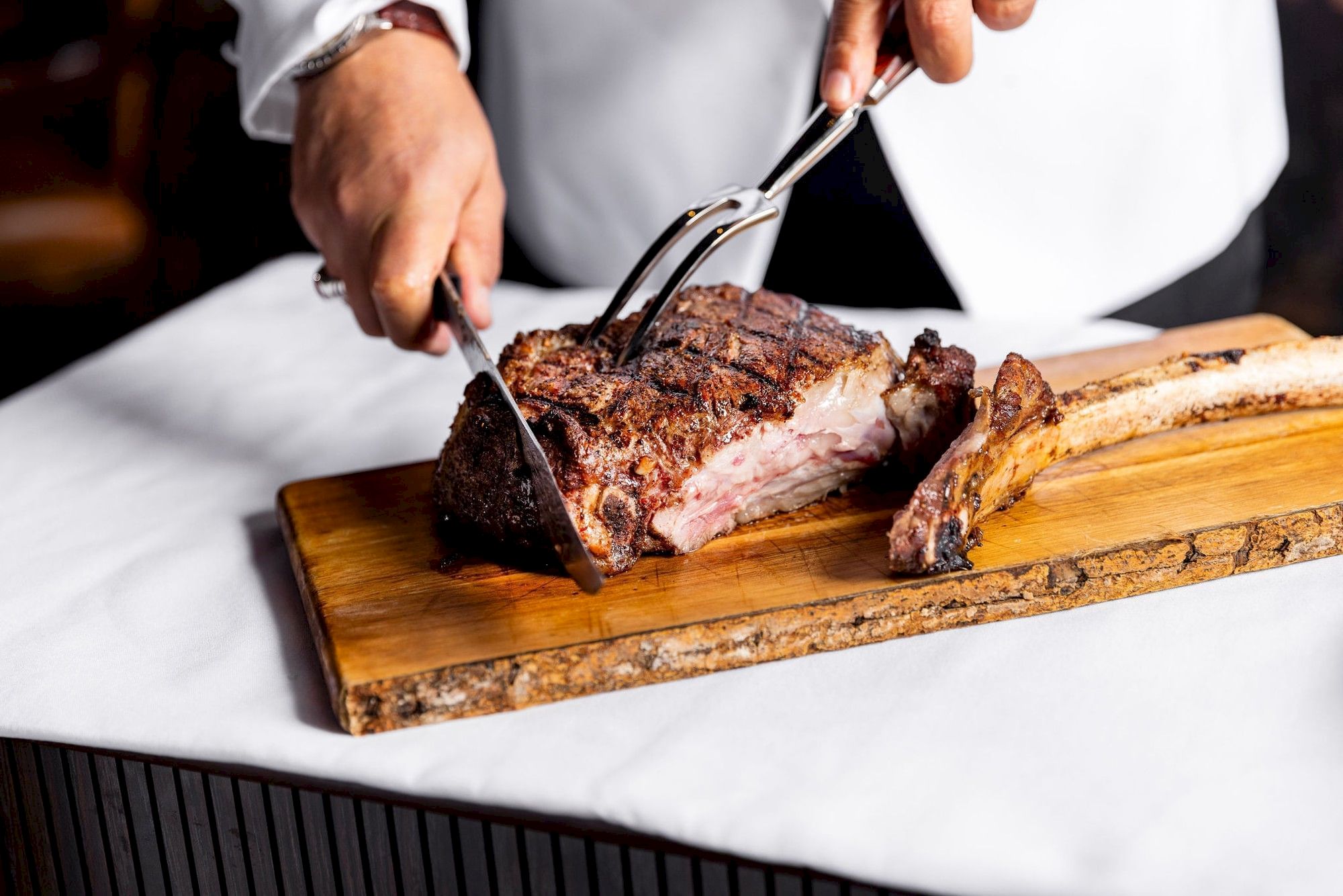 A chef slices a perfectly seared steak on a wooden board with a crusty crust and a wine-brown glaze.