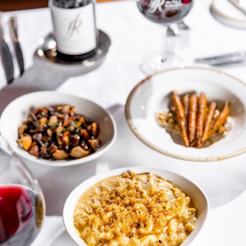 A fine dining table with wine and a trio of dishes: creamy risotto, almonds and herbs, and a savory bean/vegetable medley, plus wine glasses.