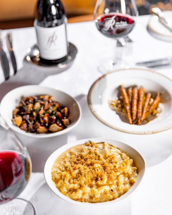 A fine dining table with wine and a trio of dishes: creamy risotto, almonds and herbs, and a savory bean/vegetable medley, plus wine glasses.