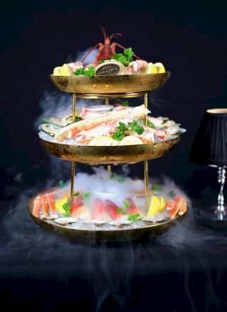 A stacked burger-and-sushi hybrid with bright fillings, layered between a bun-like top and bottom, set on a dark background.