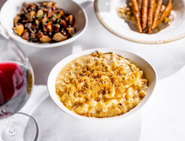 A refined table with wine and three bowls: creamy mashed? corn? and a nutty mix&mdash;plus a bottle and glass; a chic, intimate dining setup.