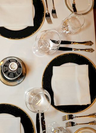 A formal table setting with black chargers, white napkins, crystal glasses, and polished silverware arranged neatly around a centerpiece.